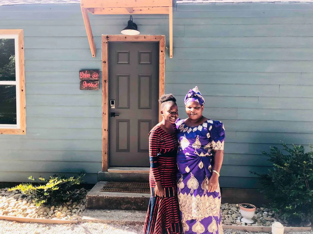 The front entryway of the property, with two women in traditional attire greeting each other. The decorative sign and the welcoming atmosphere suggest this is a place for memorable arrivals, family gatherings, and a sense of community.