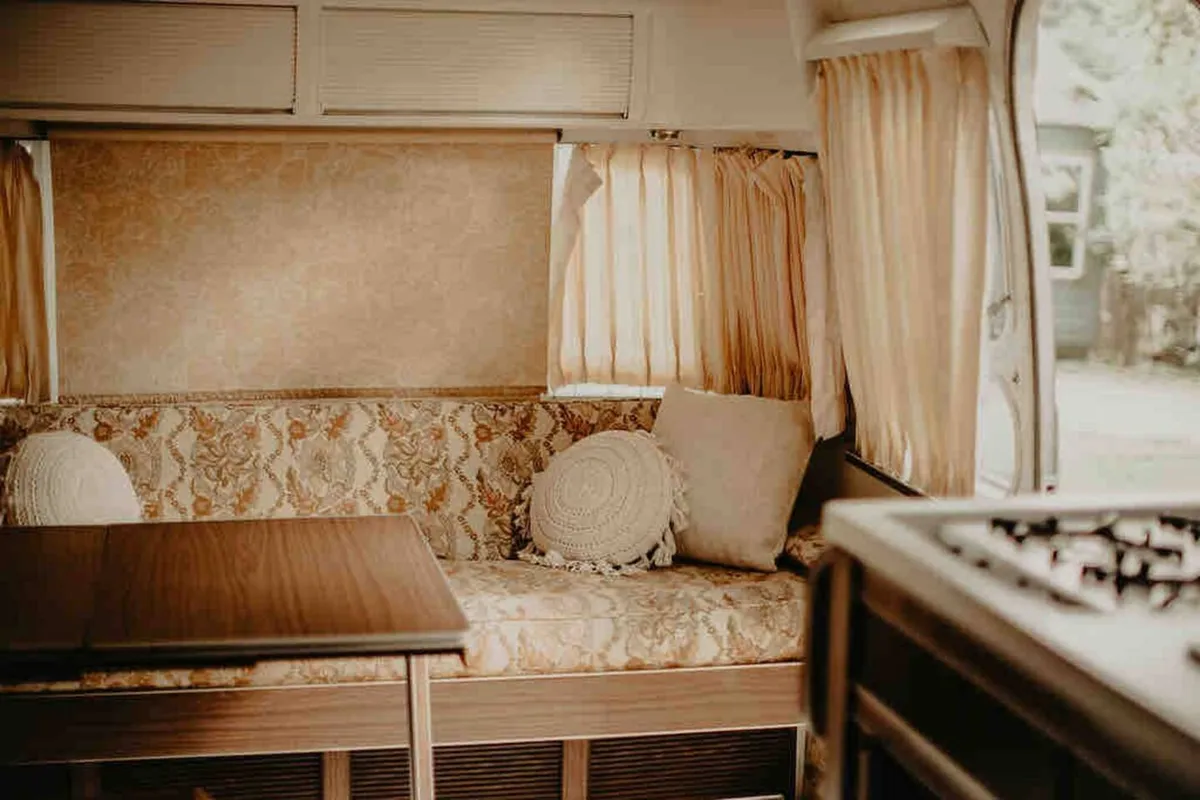 A plush couch surrounded by decorative pillows, with a wooden table in front, set in a nostalgic and intimate environment. The layout encourages close conversations, shared meals, or quiet relaxation as a group.