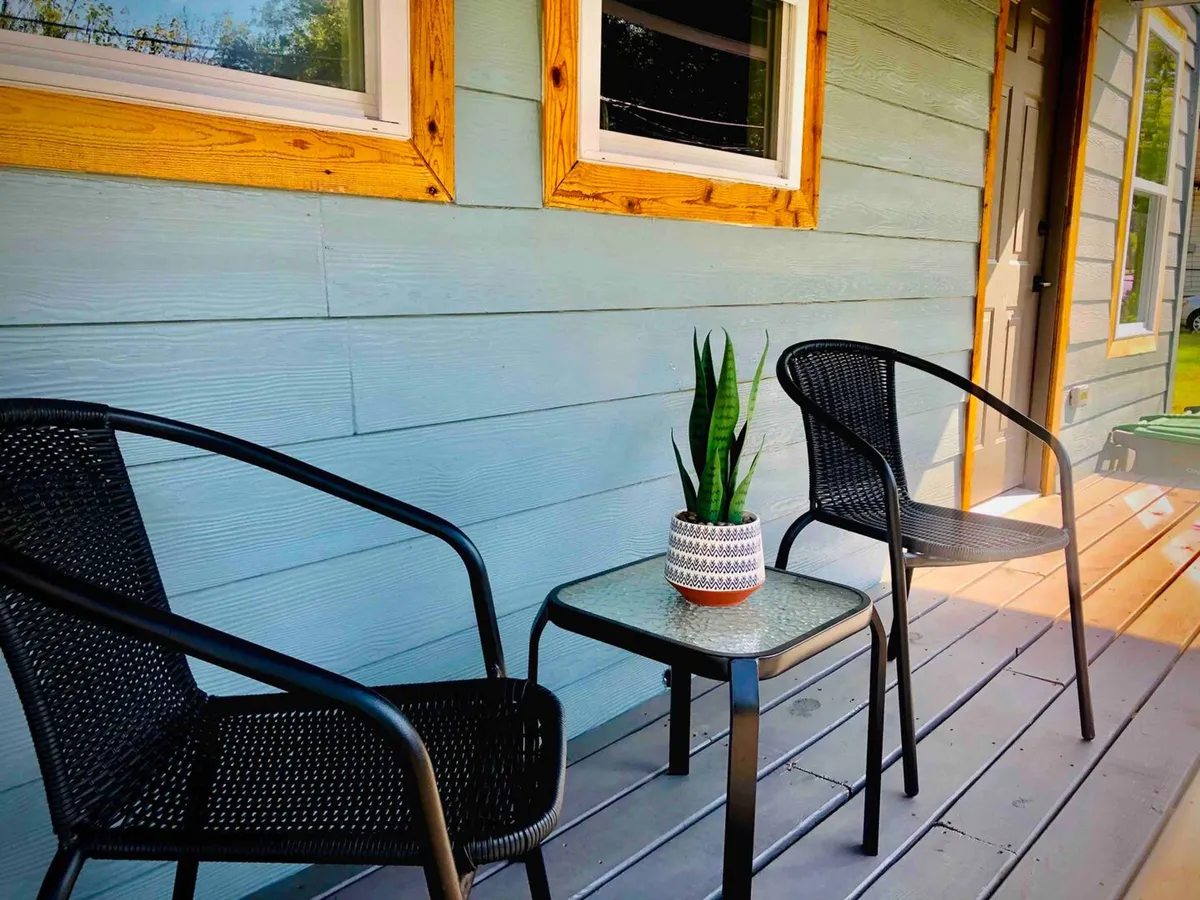 A small but thoughtfully arranged patio with two black chairs, a glass-top table, and a decorative plant, set under the open sky—ideal for quiet moments or intimate conversation.