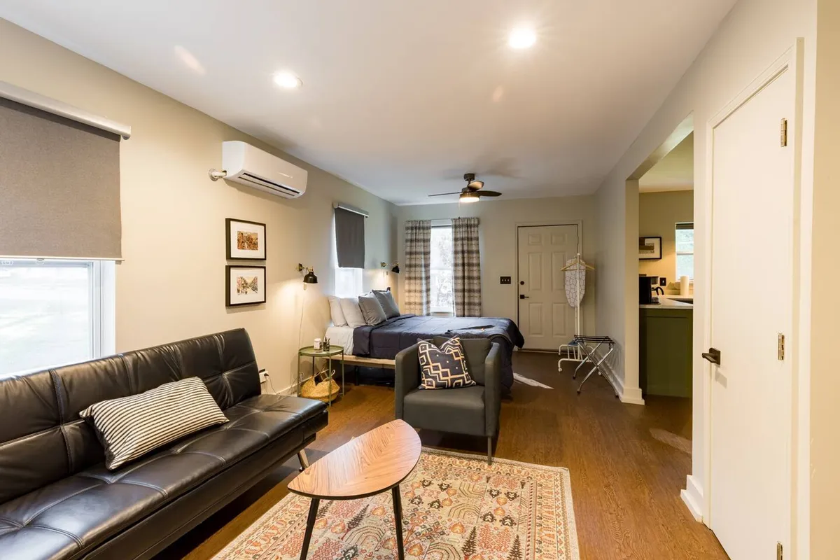 A stylish studio interior with a cozy sofa, comfortable bed, coffee table, and locally-inspired artwork, all bathed in natural light from a large window. The inviting space is perfect for couples to relax together, enjoy intimate conversations, or start the day with coffee.