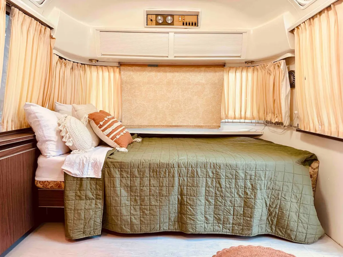 A cozy interior featuring a bed with a green quilt and decorative pillows, framed by soft curtains. The mood is tranquil and inviting, ideal for rest and relaxation after a busy day.