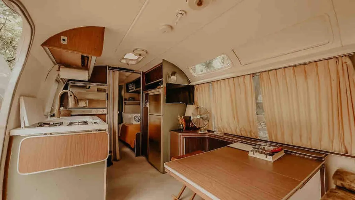 A compact kitchen area with a dining table, curtains, and a refrigerator, evoking the charm and practicality of a kitchenette. The space is designed for sharing meals or preparing snacks in a welcoming, home-like atmosphere.