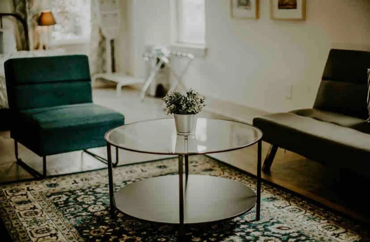 A welcoming living space with a green armchair, gray sofa, glass coffee table, and a potted plant, arranged to encourage conversation and shared activities. The room feels open, comfortable, and ready for entertaining.
