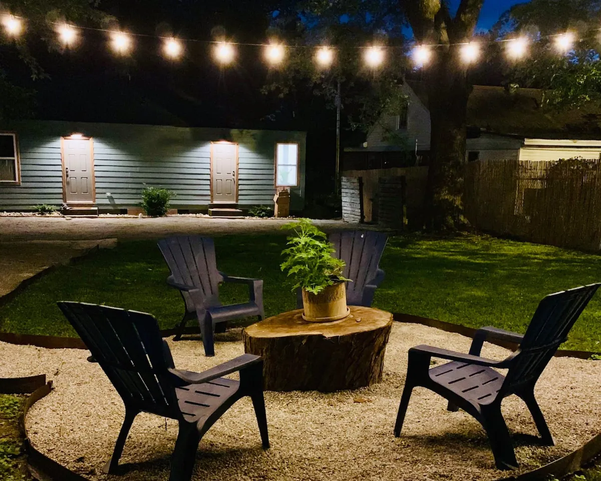 This image features a welcoming outdoor setup with string lights, an inviting fire pit surrounded by Adirondack chairs, and a potted plant, creating a cozy atmosphere ideal for group gatherings and evening relaxation.